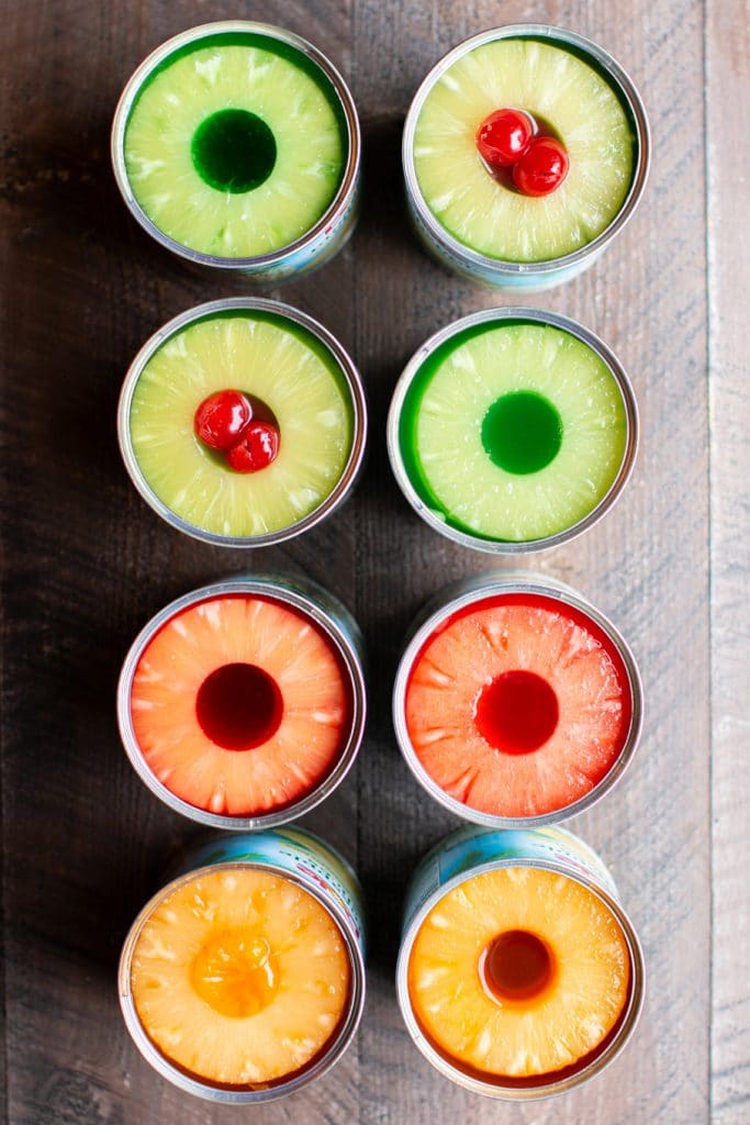 cans of pineapple with multi colored jello in them.