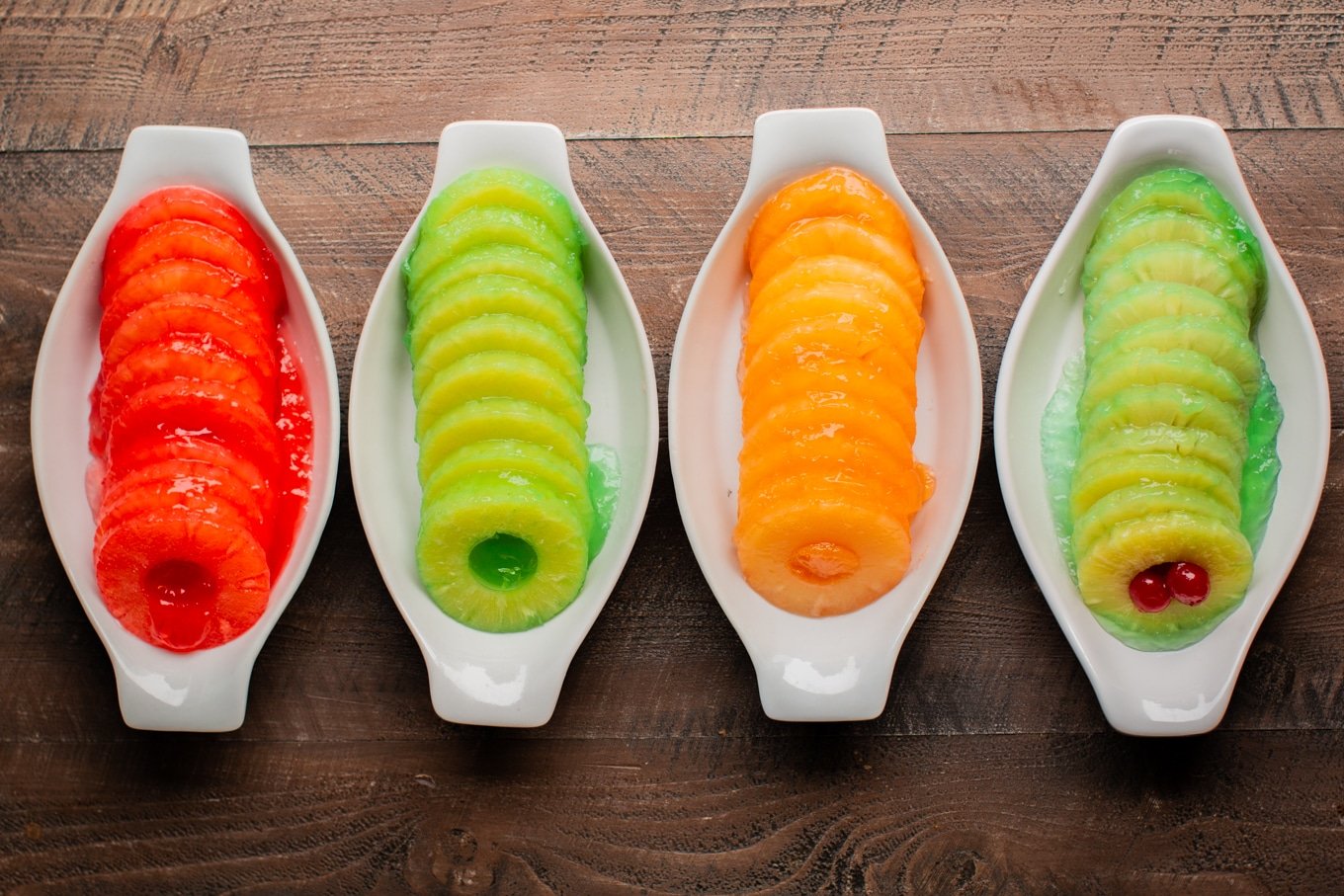 4 bowls with 3 different colors of jello with pineapple rings.