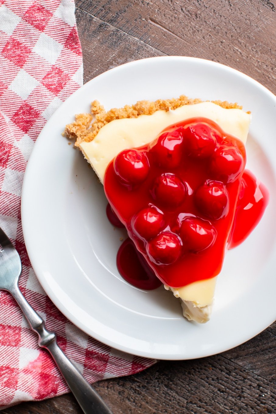 slice of cream cheese pie with cherries on top.