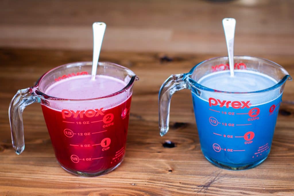 2 measuring cups. One with red jello mix and one with blue.