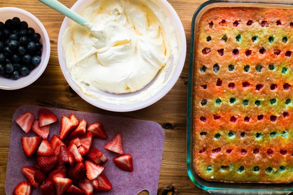 Frosting in a bowl, strawberries on cutting board. Cake on the side.