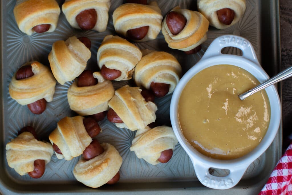 pigs in a blanket on sheet pan with mustard in white bowl