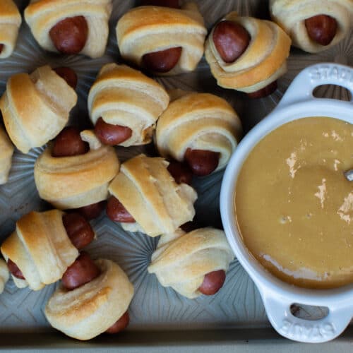 pigs in a blanket on sheet pan with mustard in white bowl