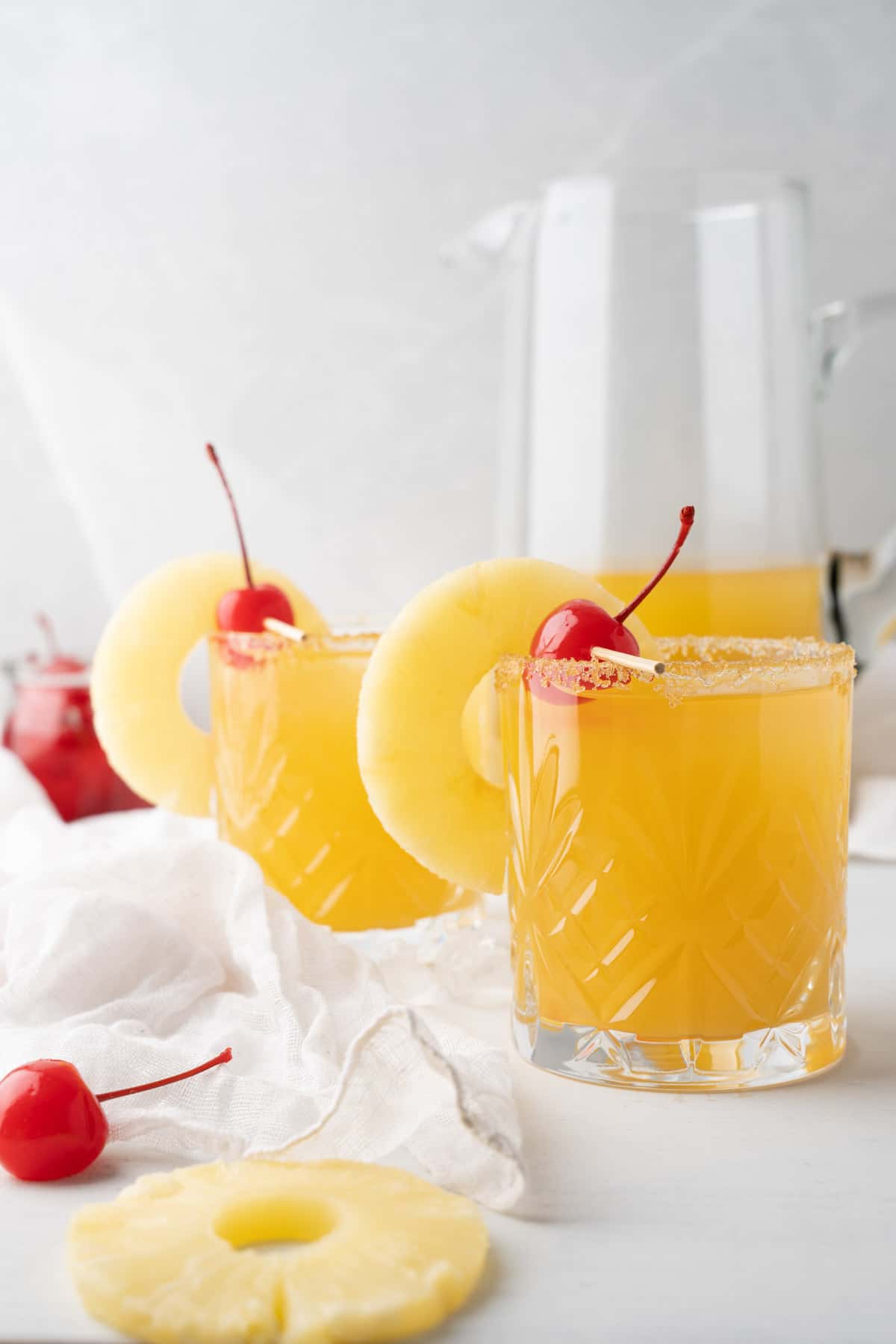 2 pineapple upside down cake cocktails with cherries and pineapples in them
