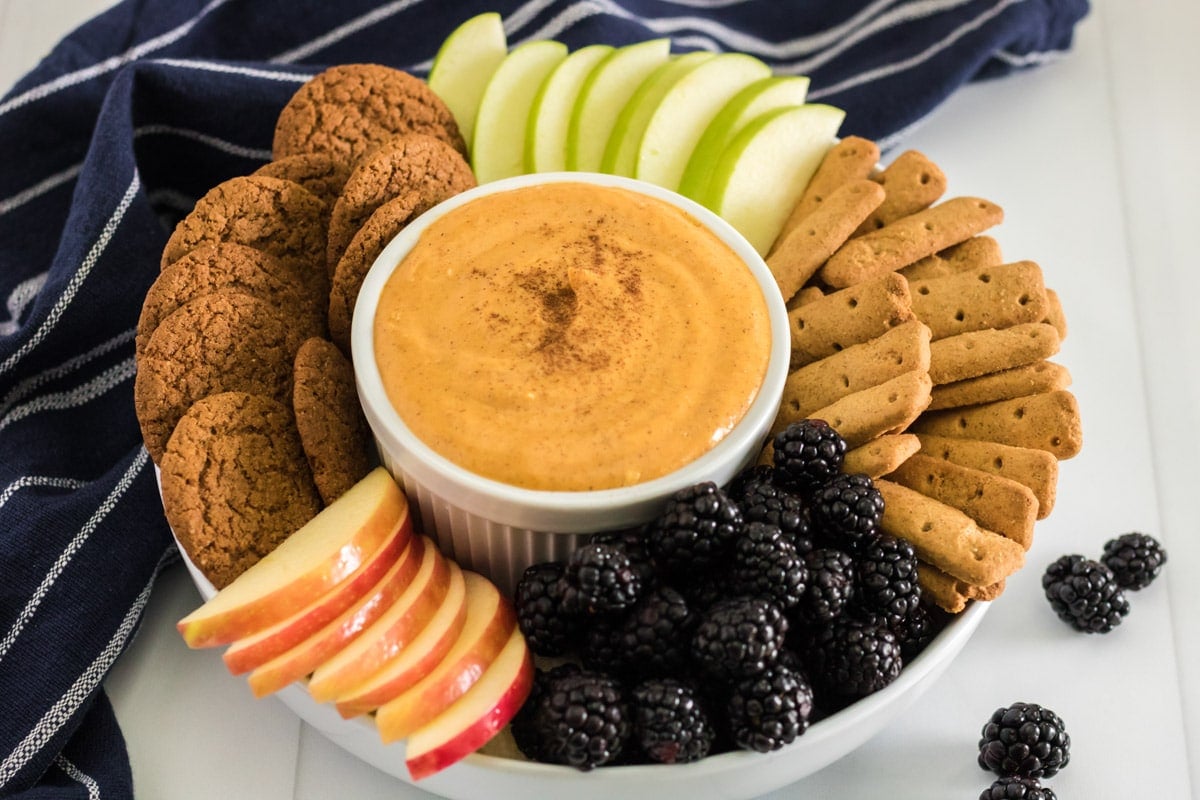 pumpkin dip with an assortment of cookies and fruit around it.