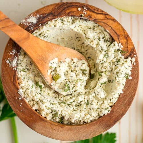 Homemade ranch mix in a wooden bowl with a small wooden spoon scooping some.