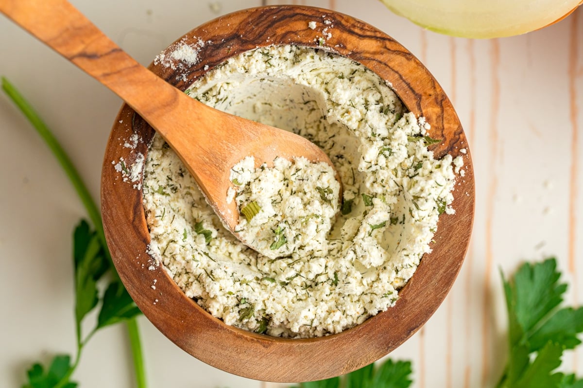Homemade ranch mix in a wooden bowl with a small wooden spoon scooping some.