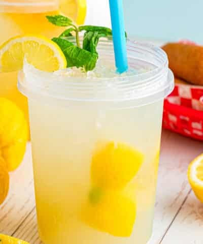 A plastic jar filled with lemonade with a blue straw, a lemon wedge, and mint leaves.