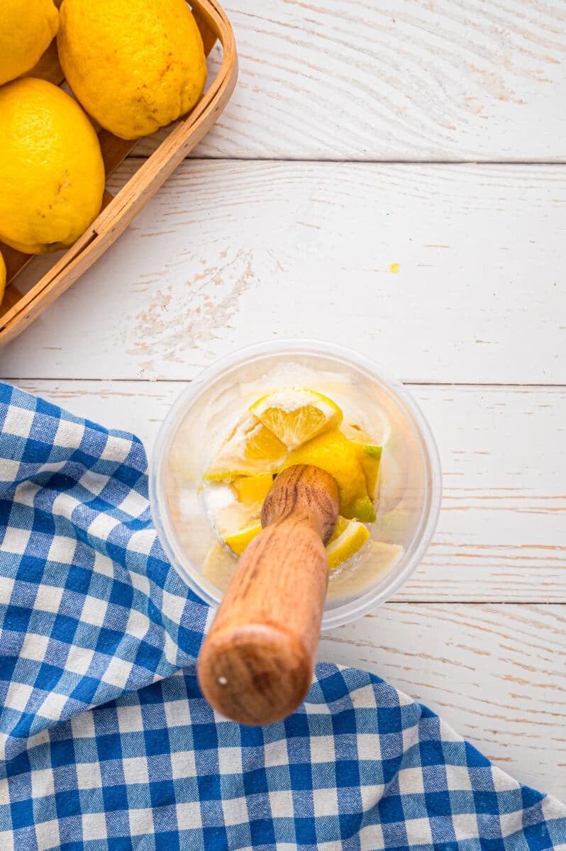 A muddler in a plastic jar of lemons and sugar.