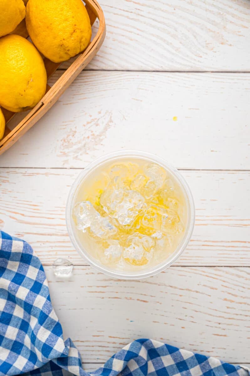 Ice and water added to a plastic jar of muddled lemons and sugar.