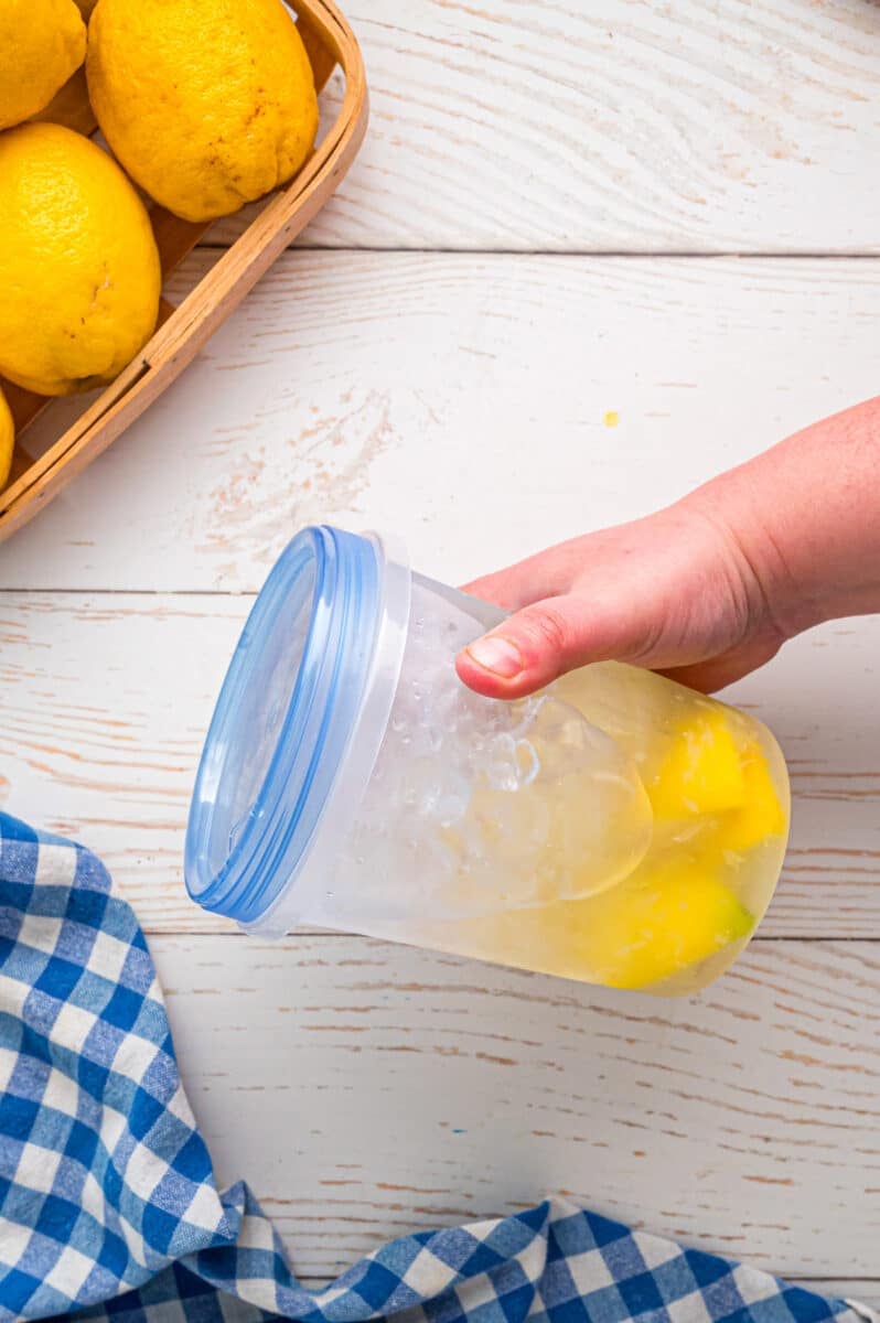 A hand holding a plastic jar of lemonade to shake it up.